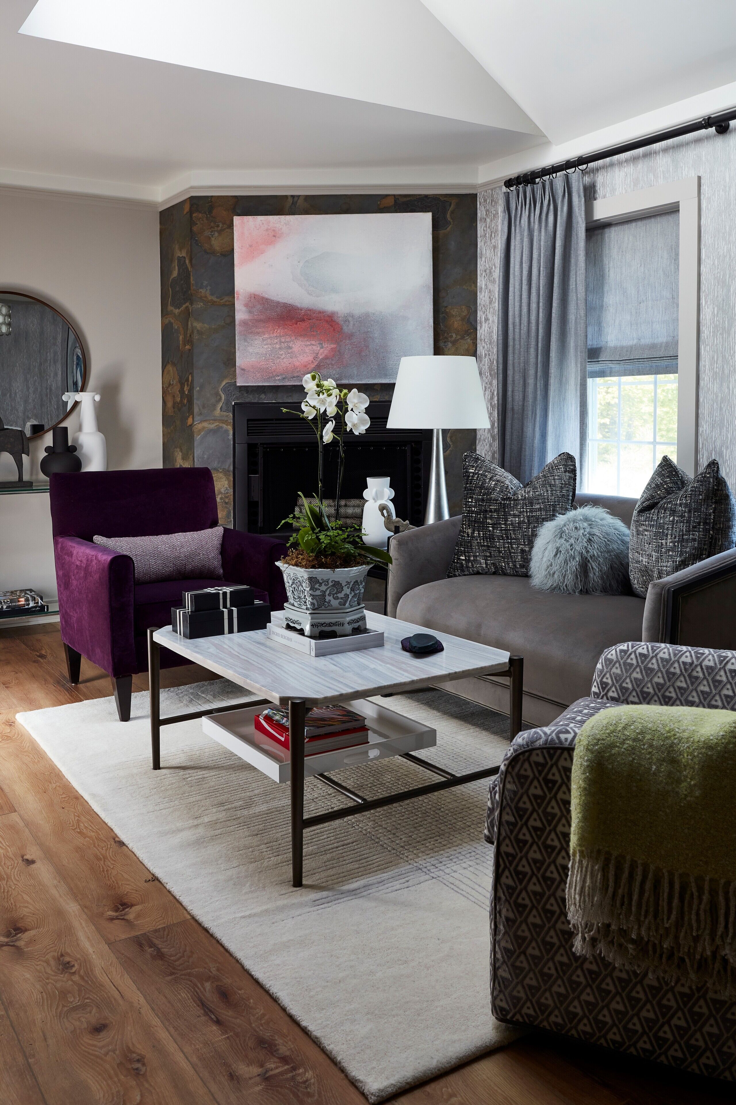 A modern living room with a purple armchair, a grey sofa, a coffee table, and a fireplace.