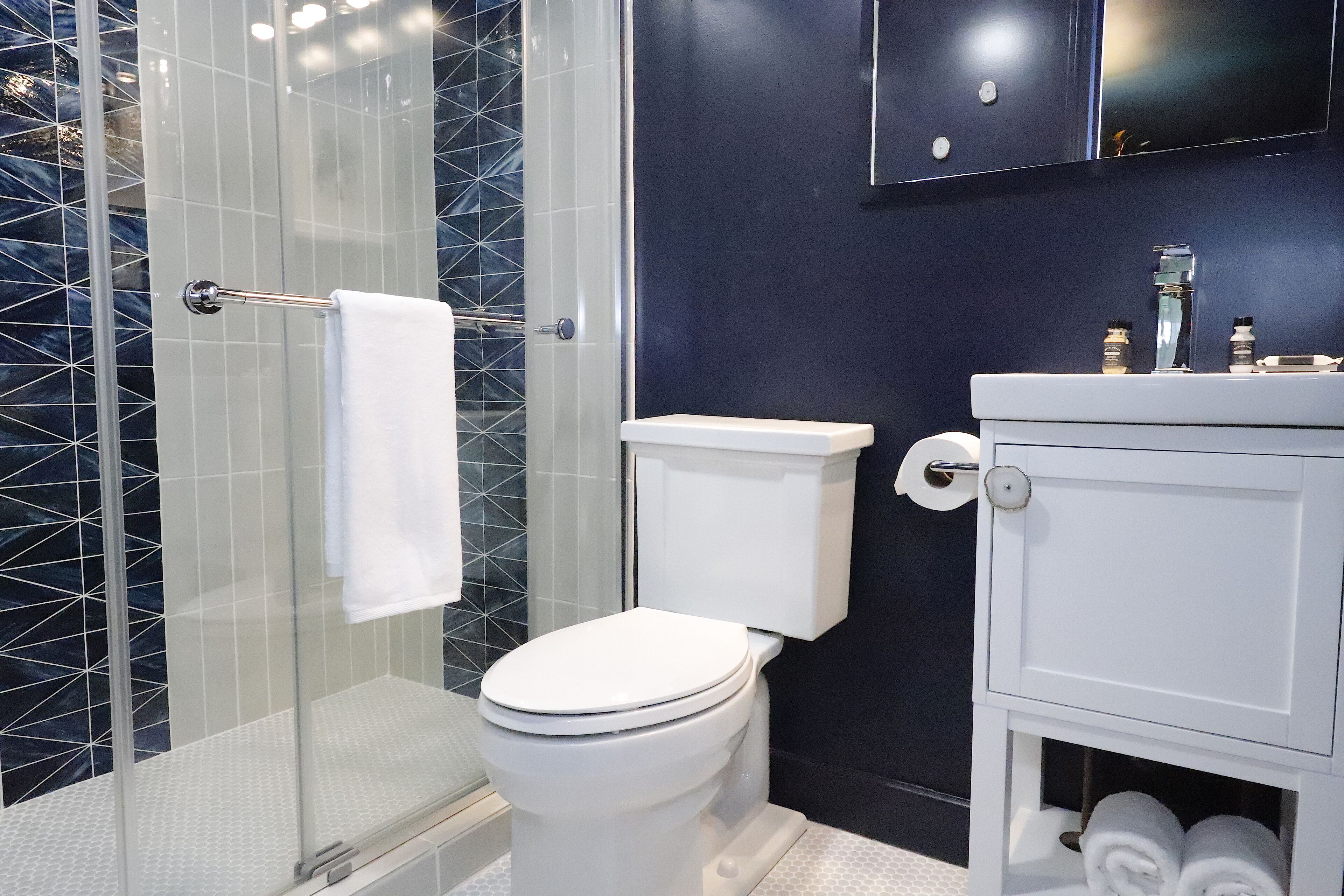 Un baño moderno con cabina de ducha de vidrio, inodoro y tocador blancos con espejo.