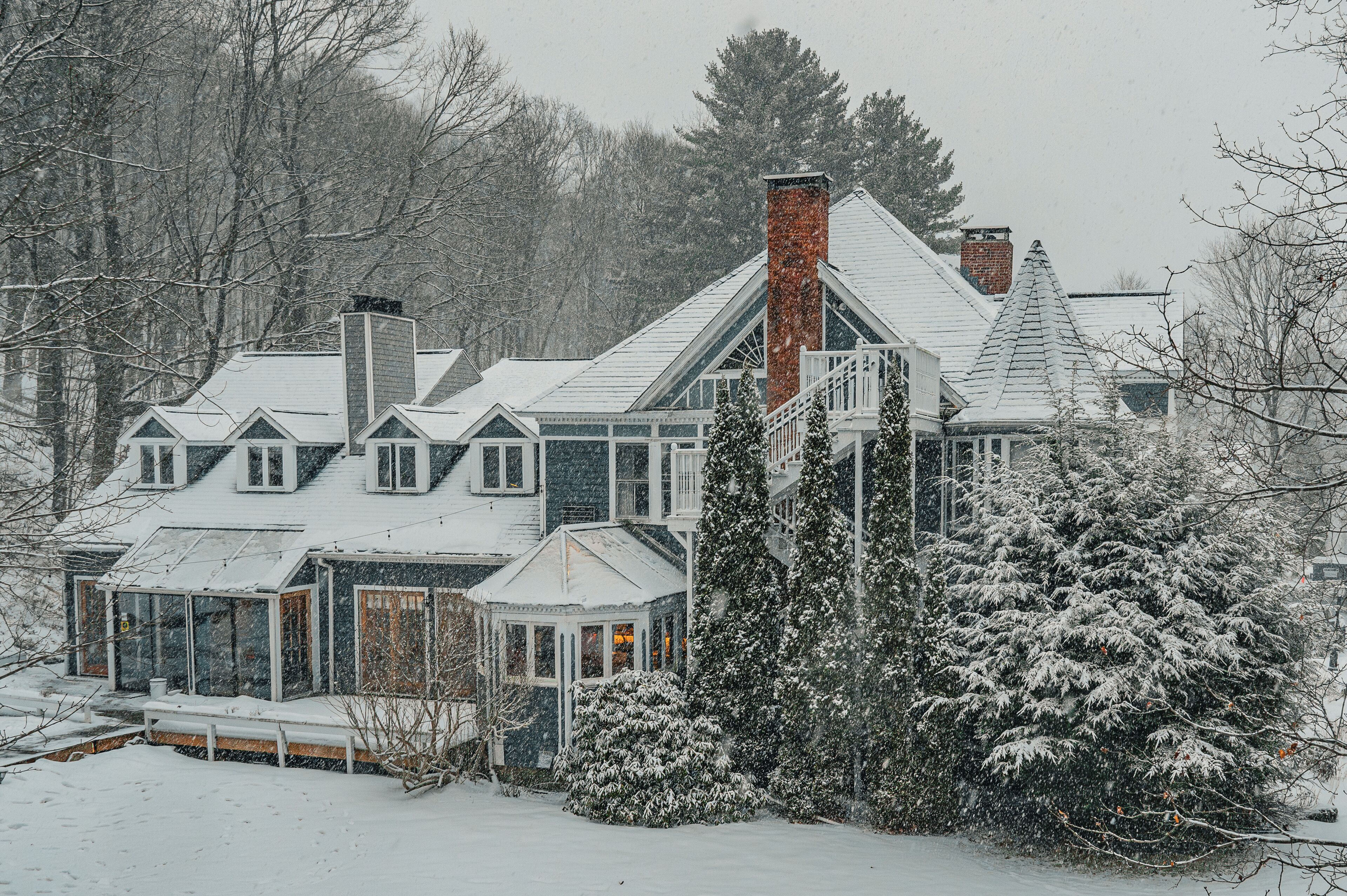 A large, multi-story house with a prominent chimney, a conservatory, and snow-covered surroundings.