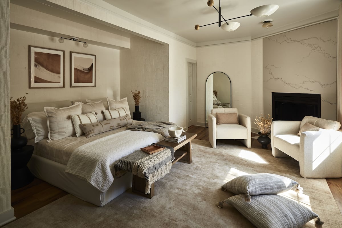 Un dormitorio con una cama grande, una zona de estar con una silla y un sofá, una chimenea y obras de arte en las paredes.
