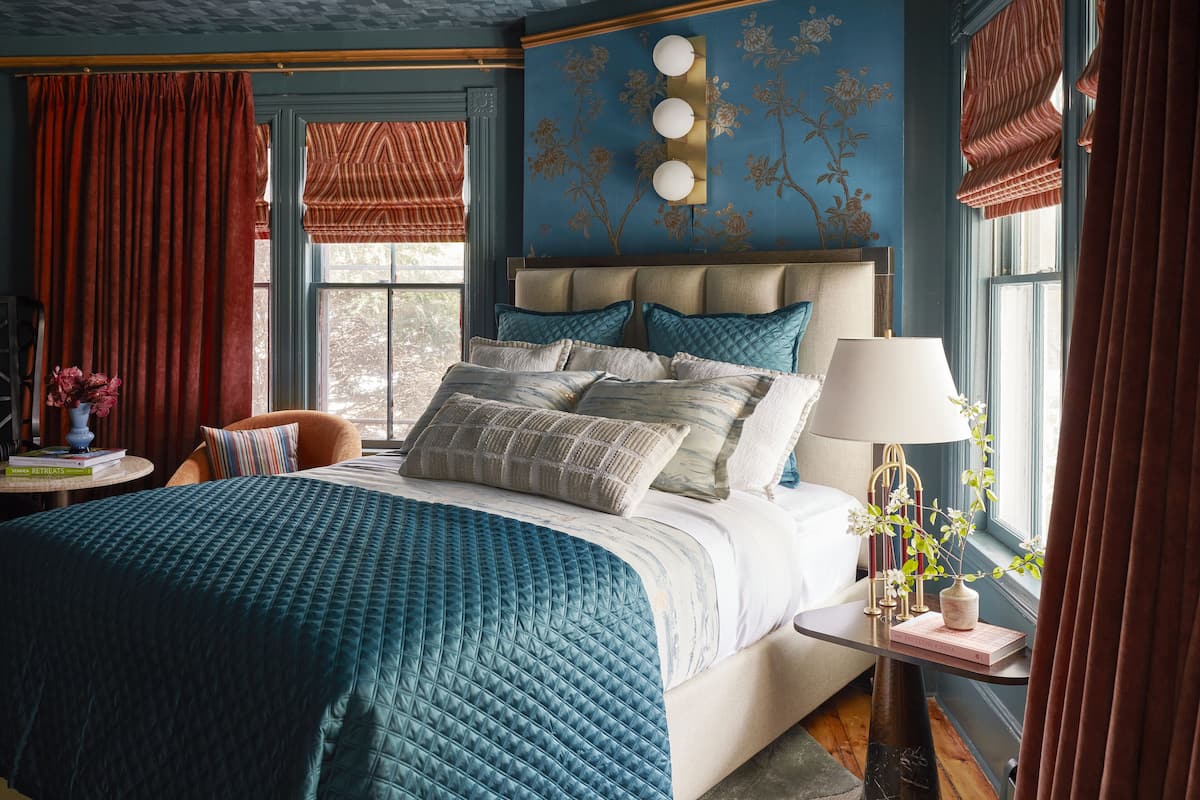 Un dormitorio con una cama grande, una mesita de noche con lámpara y una ventana con cortinas.