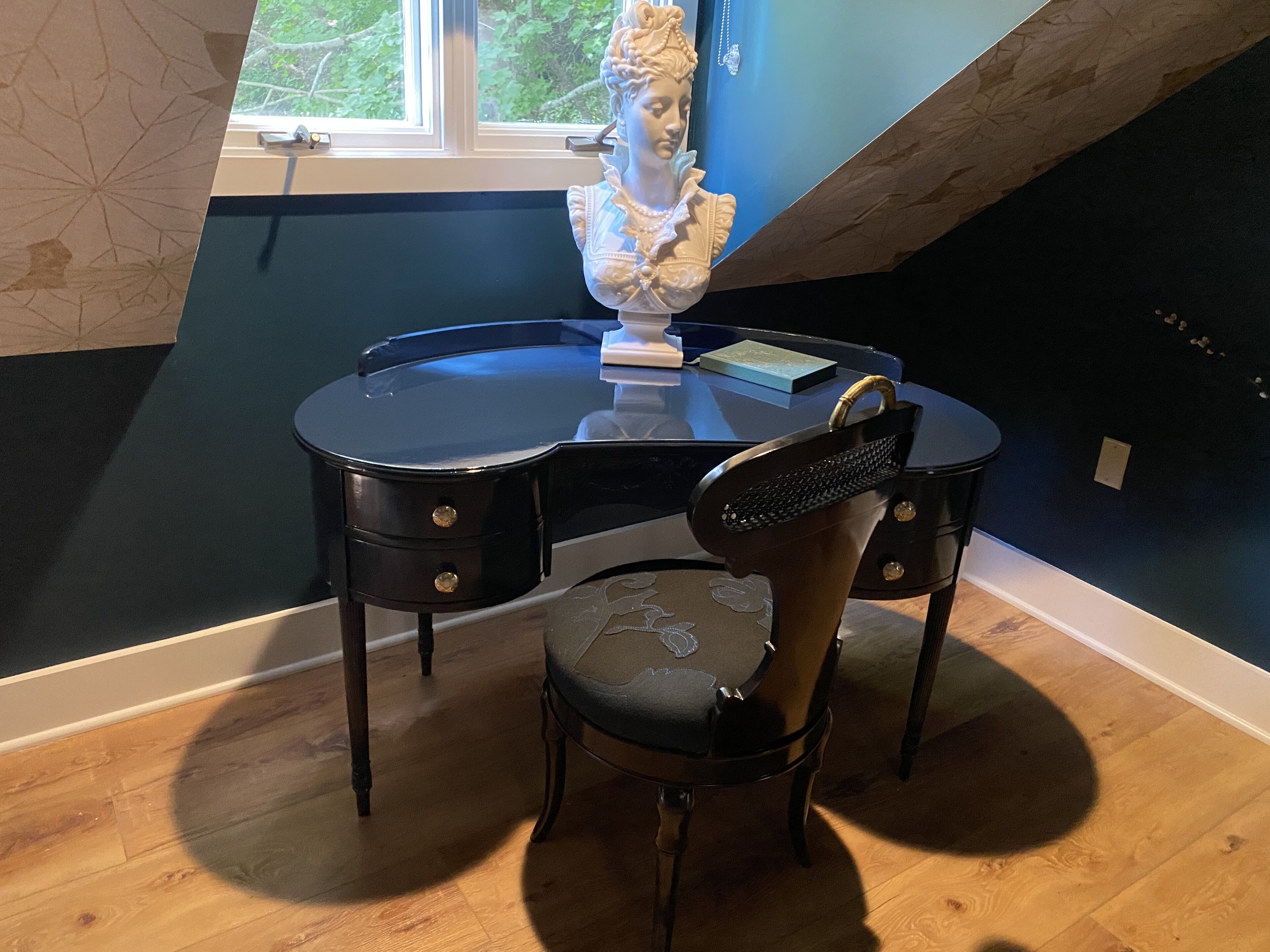 A room with a desk, chair, and a bust sculpture.