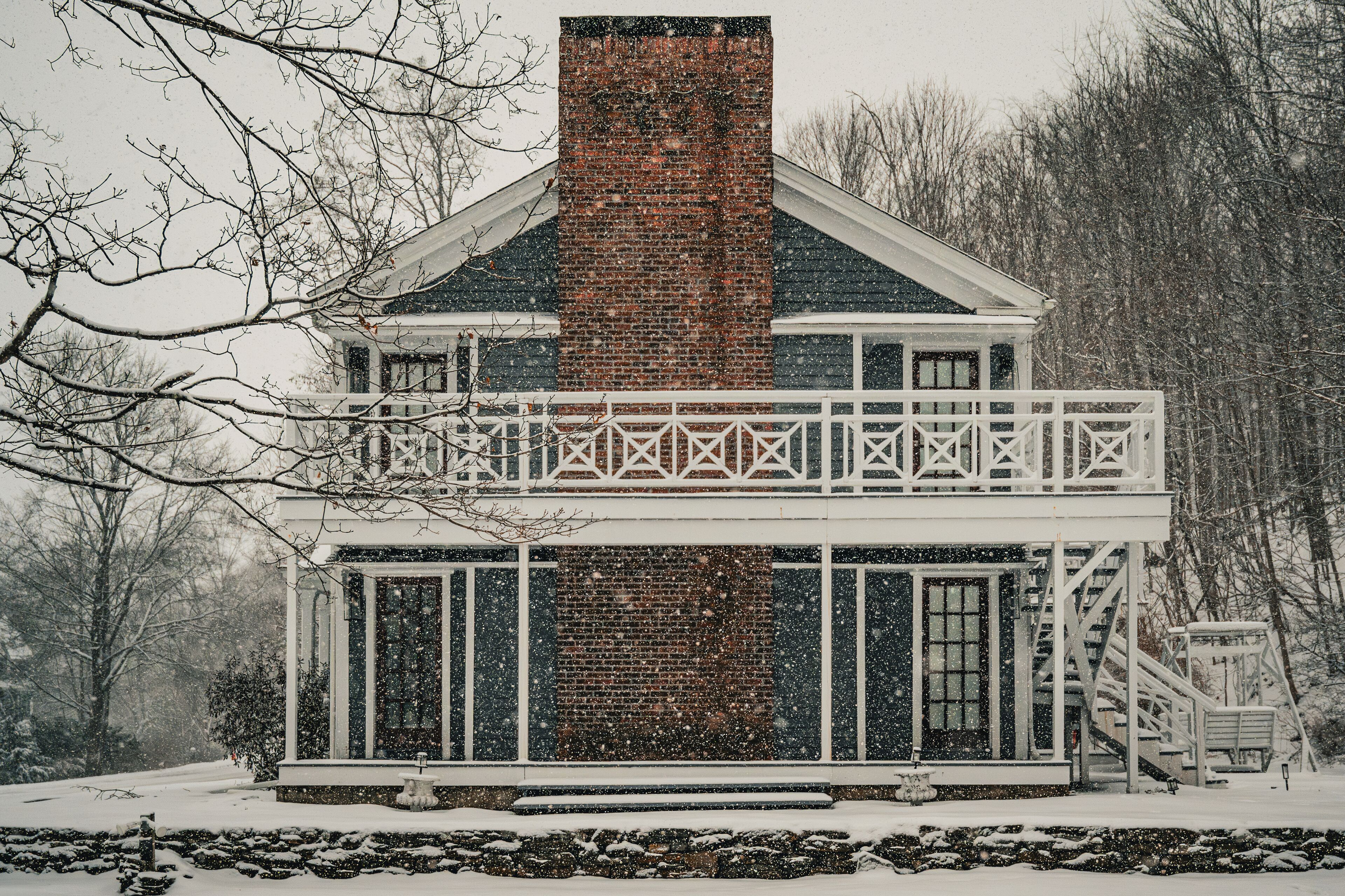 A snow-covered building with a brick chimney, white railings, and a porch.