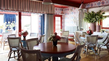 A dining area with wicker chairs, a round wooden table, and a vase of flowers.