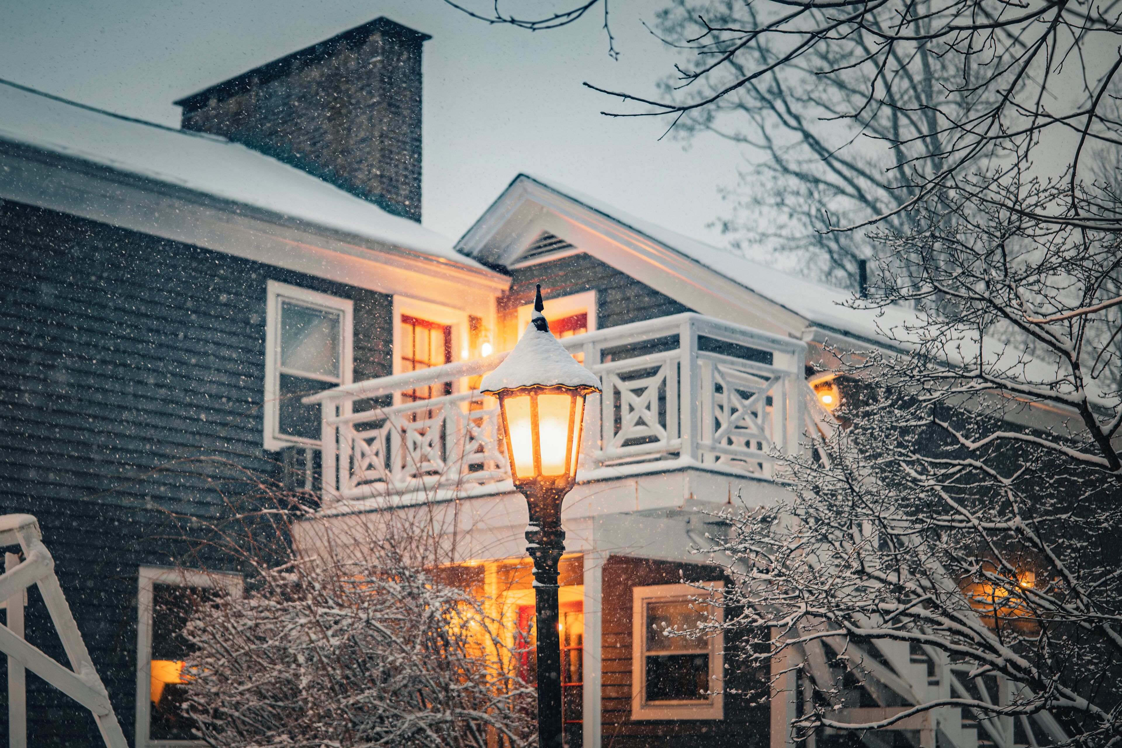 A snow-covered house with a balcony and a lit street lamp.