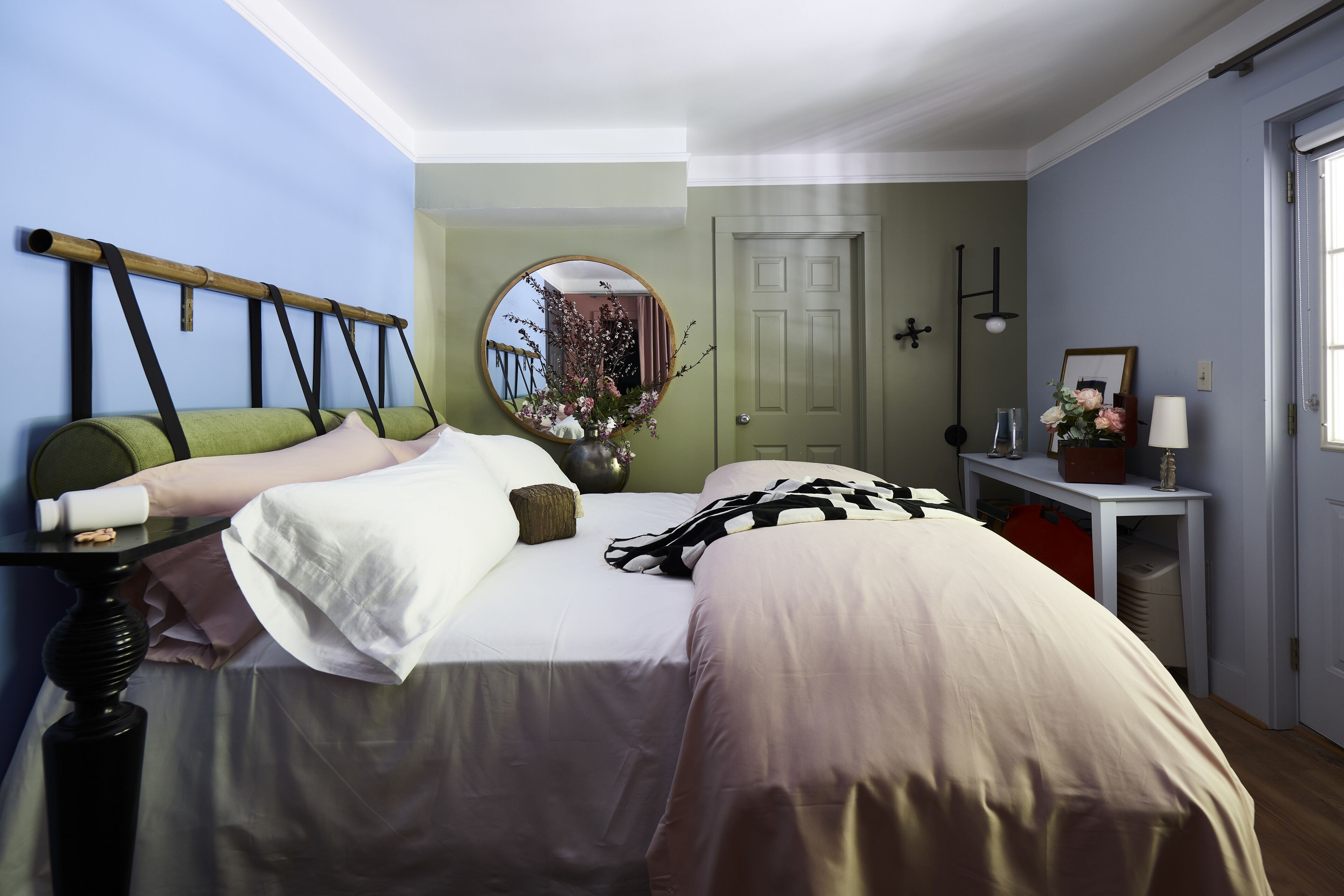 A bedroom with a bed, bedside table, lamp, and a mirror.