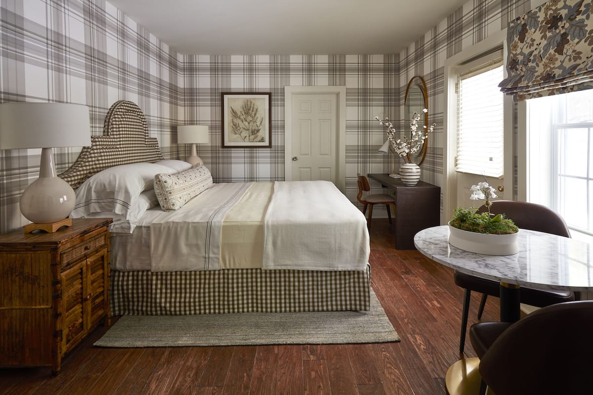 Un dormitorio con una cama grande, un aparador de madera, una mesita de noche con lámpara, una obra de arte enmarcada en la pared y una ventana con vistas.