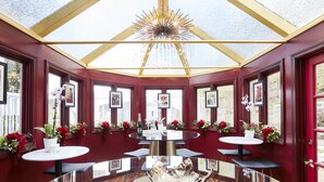 Uma sala de jantar com mesa de vidro, paredes vermelhas e quadros enquadrados.