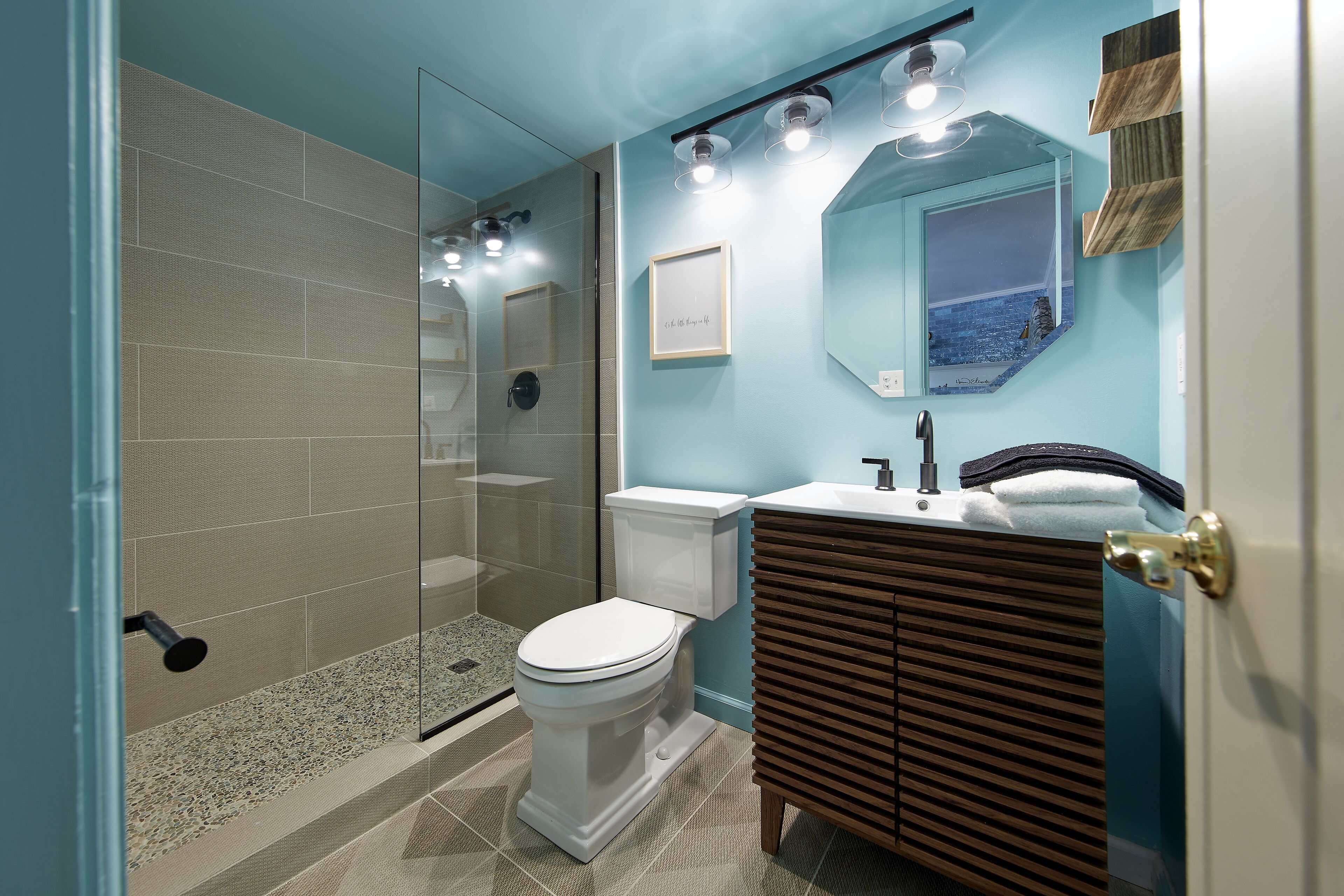 A bathroom with a glass shower enclosure, a white toilet, a vanity with a mirror, and a towel rack.
