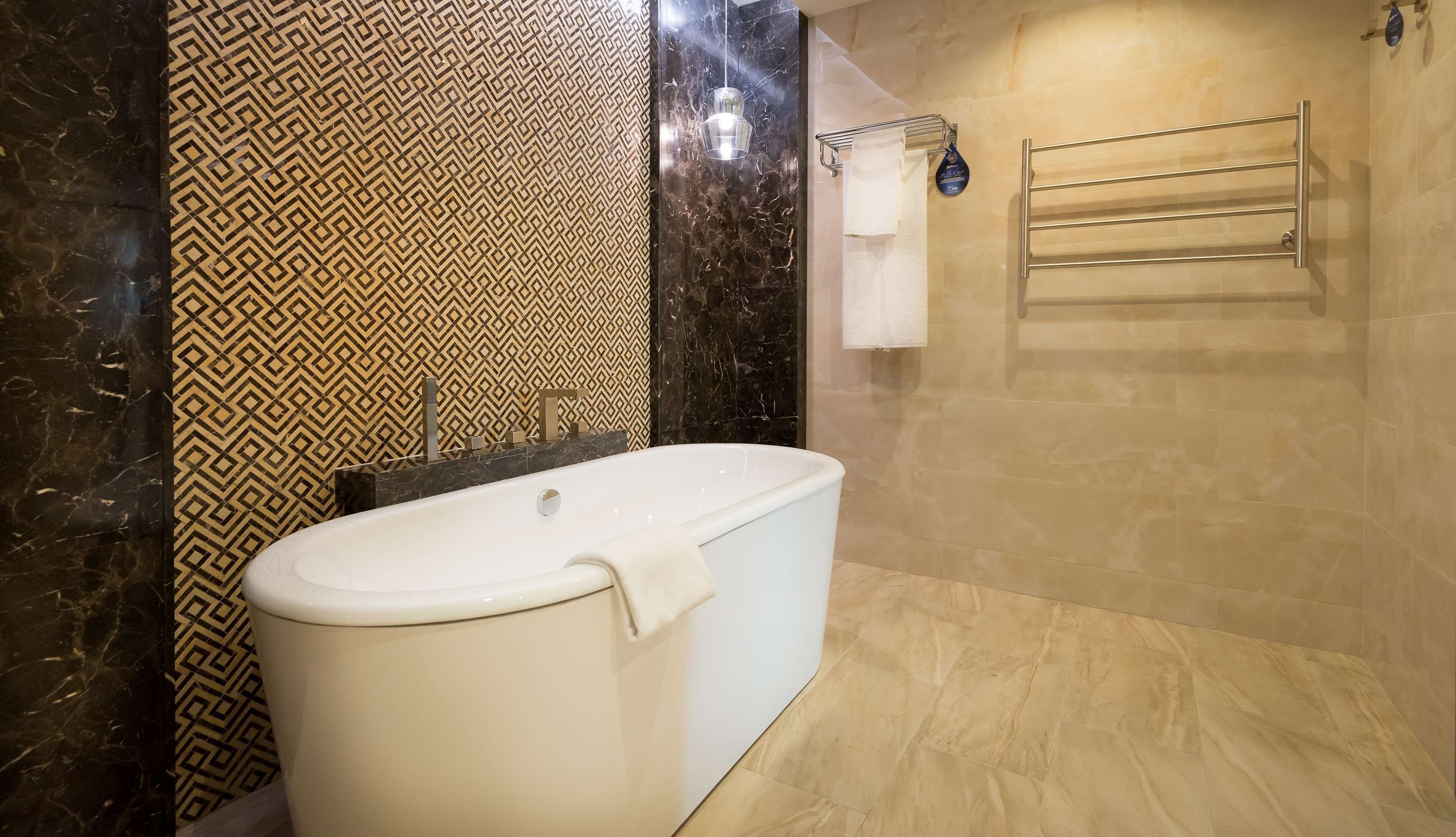 A modern bathroom with a freestanding bathtub, a towel rack, and a patterned wall.