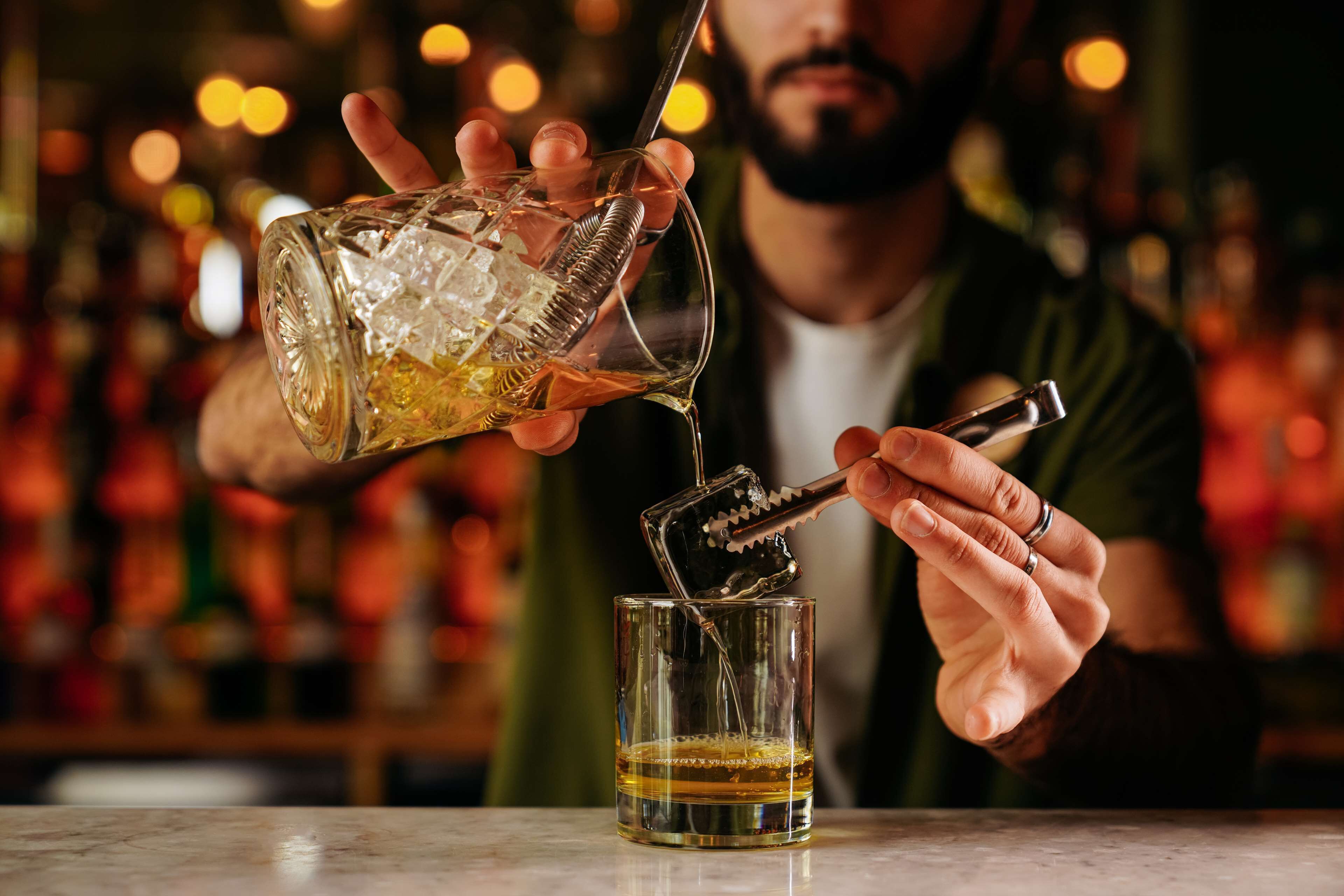 A person pouring a drink from a bottle into a glass.
