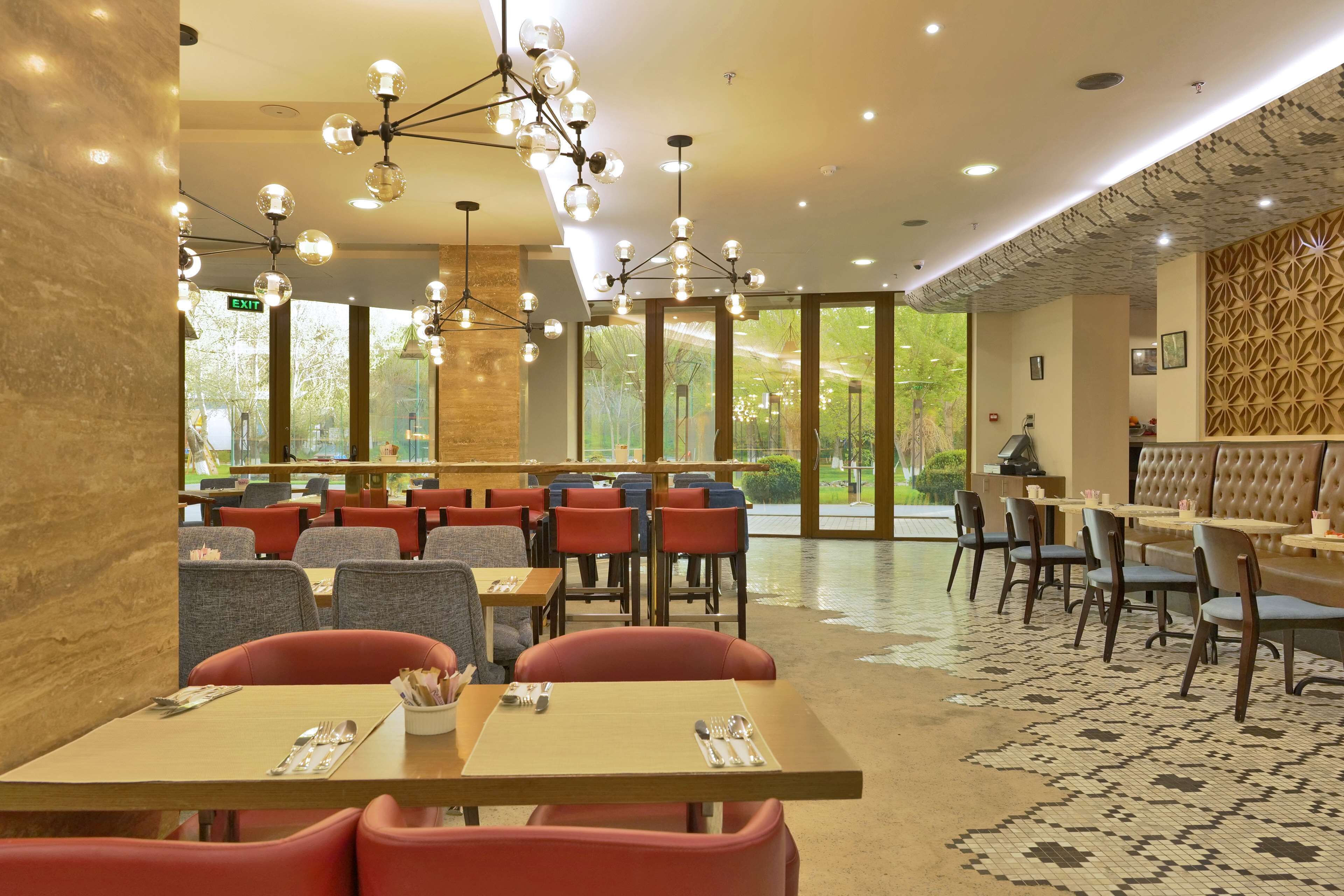 Un interior de restaurante moderno con varias mesas y sillas, un suelo con diseño y vistas a zonas verdes al exterior.