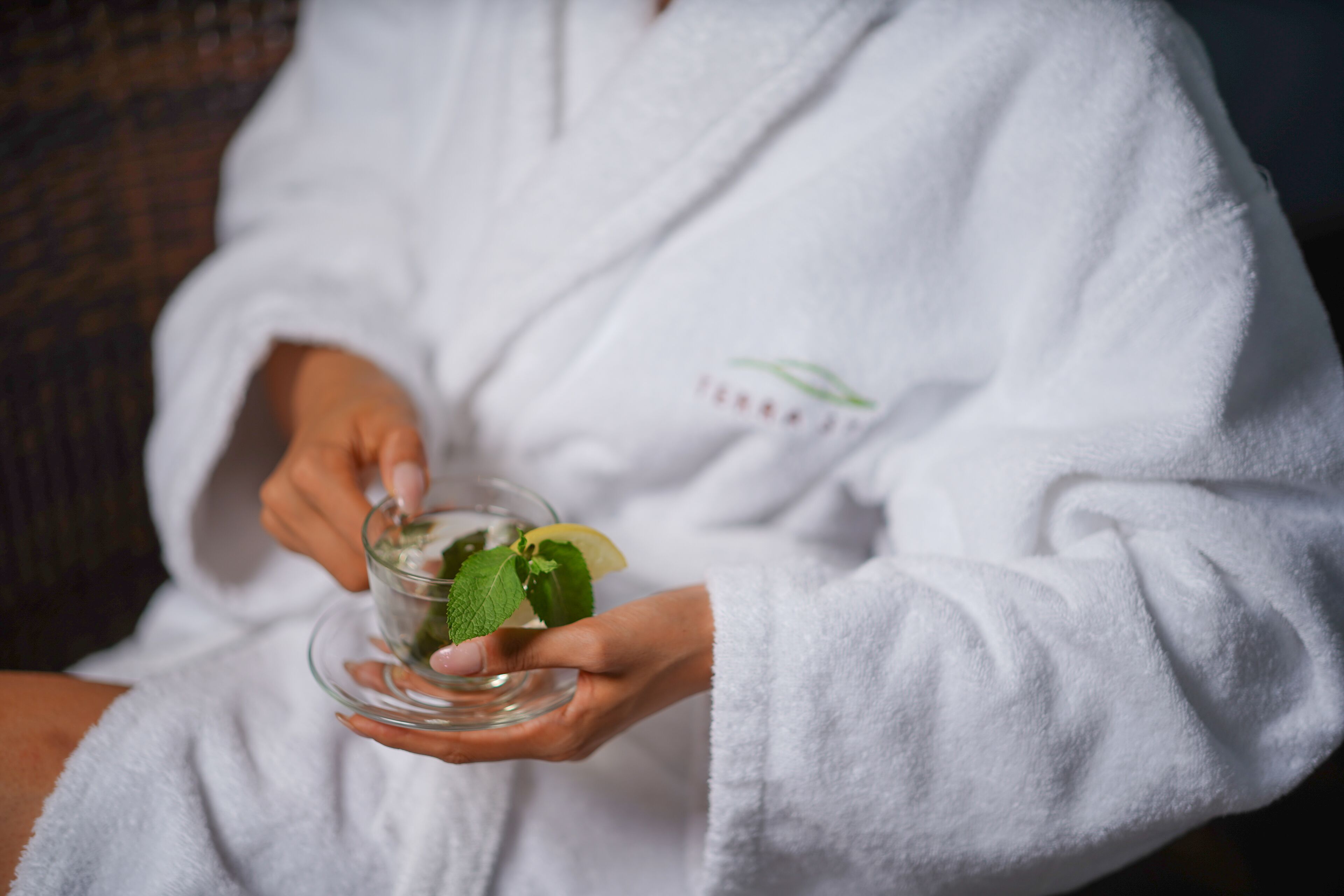 A person in a white robe holding a glass with a beverage and mint leaves.