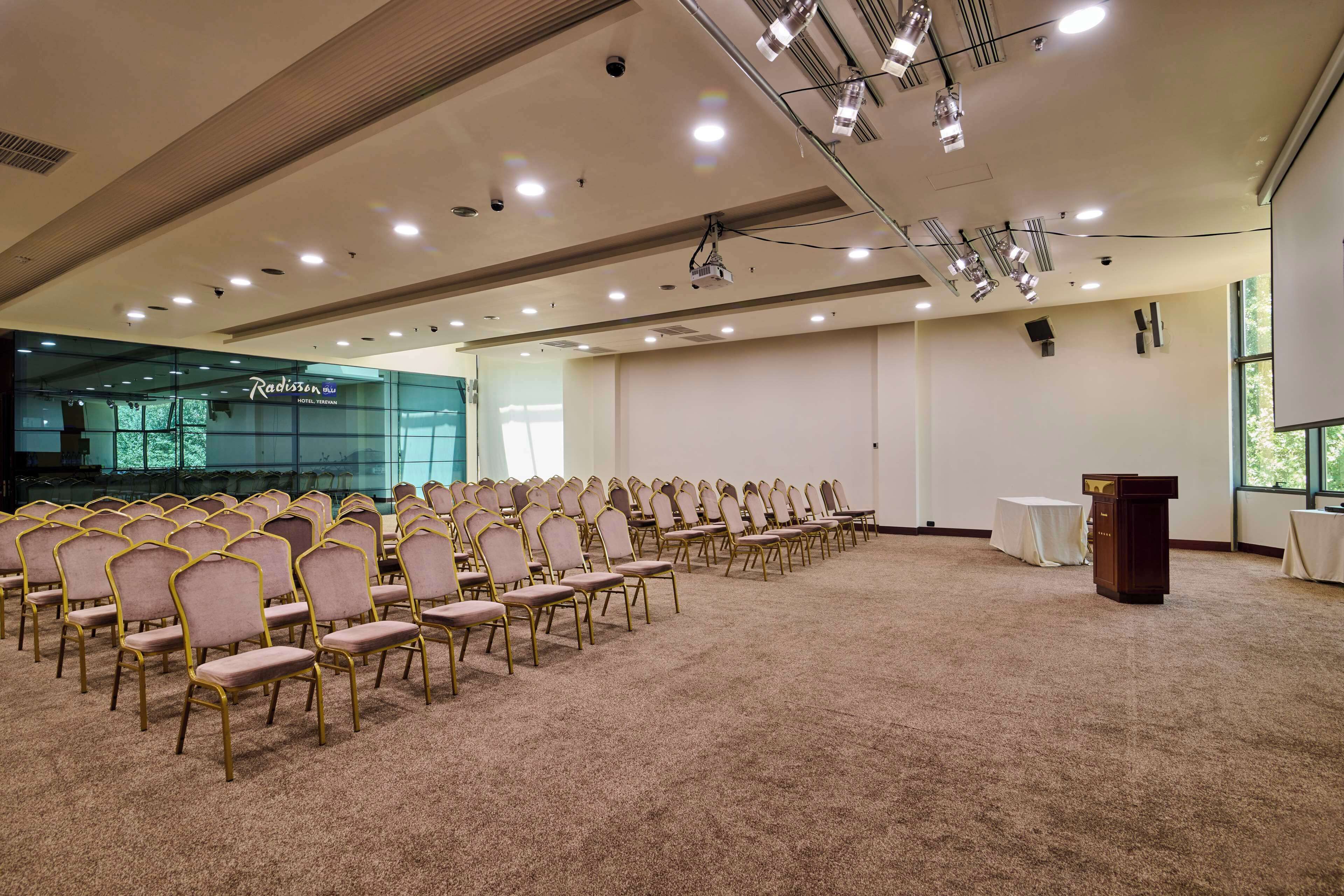 A conference room with rows of chairs, a podium, and a Radisson hotel sign in the background.