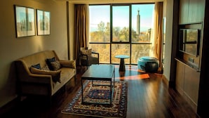 Una sala de estar moderna con sofá, mesa de centro y reposapiés, un ventanal con vistas y un televisor de pantalla plana.