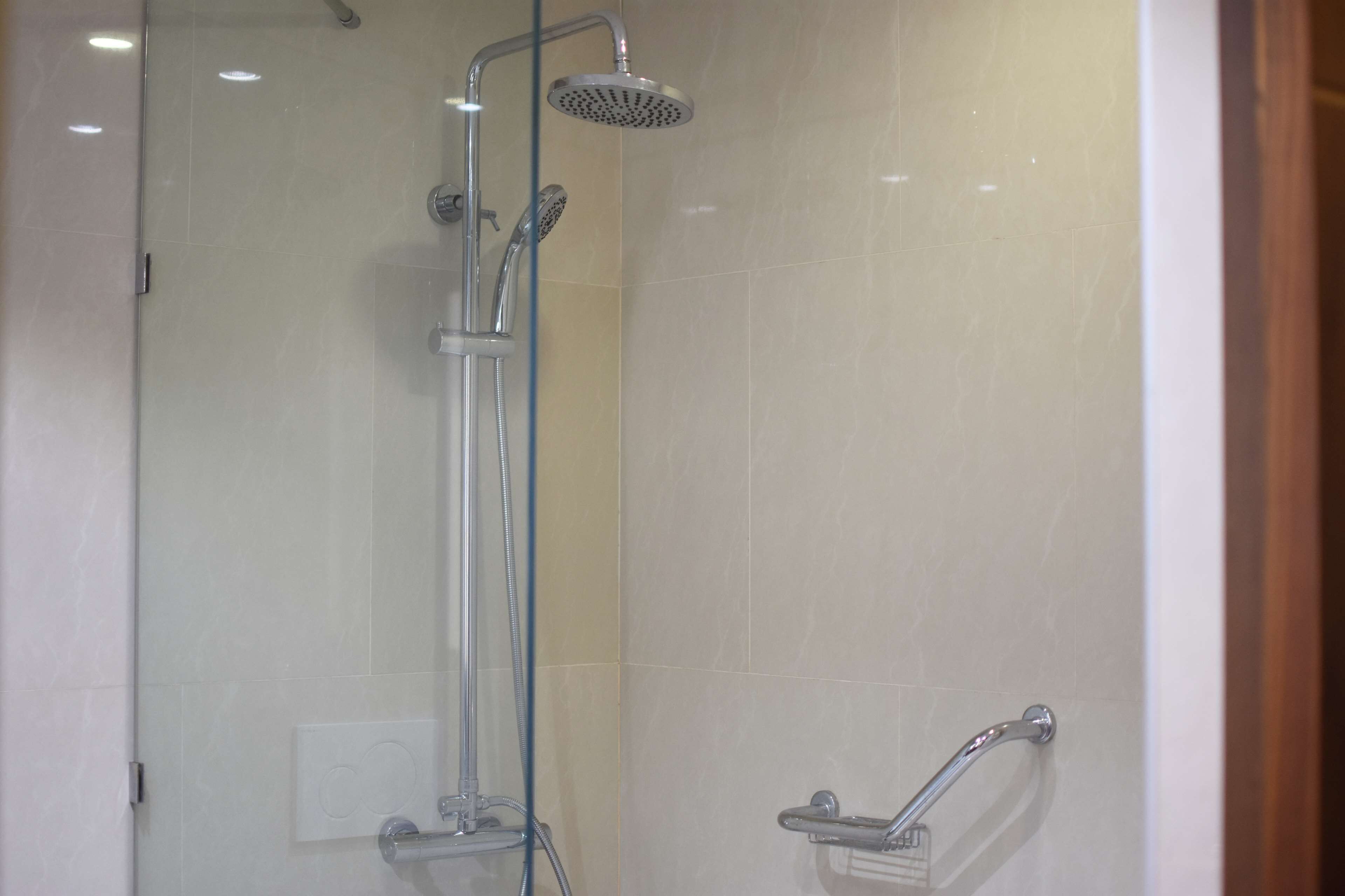 Un área de ducha con paredes de vidrio, con cabezal de ducha de mano y grifo instalado en la pared.