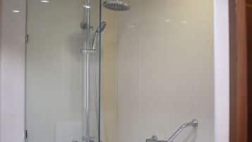 Un área de ducha con paredes de vidrio, con cabezal de ducha de mano y grifo instalado en la pared.
