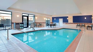 A swimming pool with a tiled deck, a sunroom with a large window, and a seating area with chairs and a table. - SpringHill Suites by Marriott Indianapolis Fishers (Fishers)