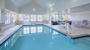 Ein großer, überdachter Pool mit klarem, blauem Wasser, umgeben von Liegestühlen und einer Sitzecke mit Fernseher.