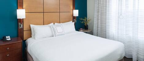 A hotel room with a large bed, wooden headboard, two bedside tables with lamps, a telephone, and a vase with flowers.