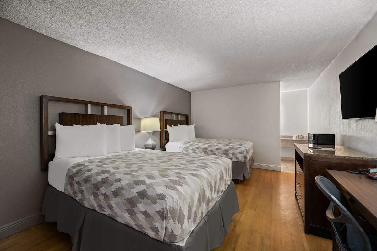 Une chambre d’hôtel avec deux lits, un bureau, une chaise, une télévision et une lampe.