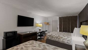A hotel room with two beds, a desk with a chair, a television, a lamp, and a microwave.