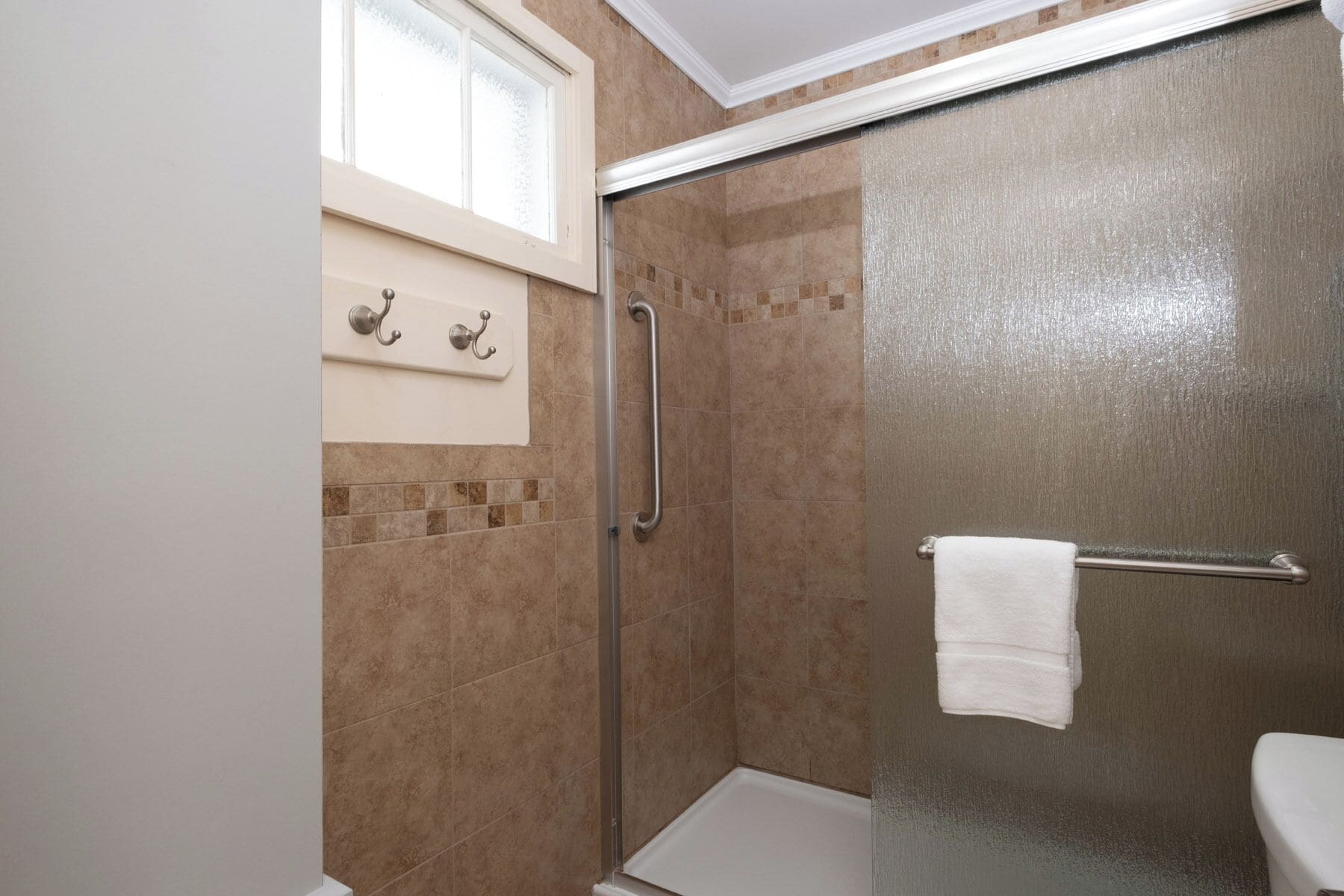 A bathroom with a glass shower door, a white towel rack, and a window above the sink.