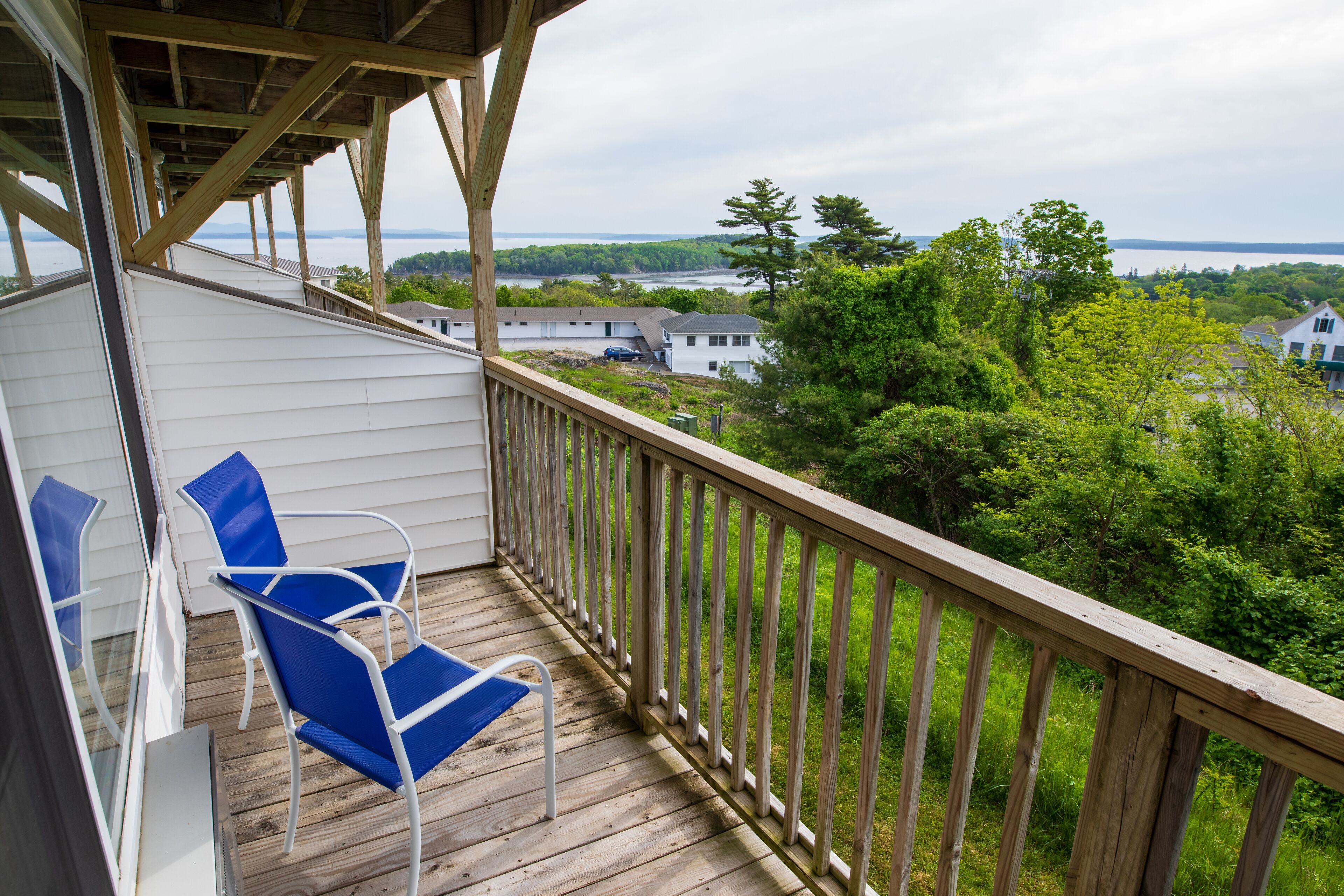 A wooden deck with blue chairs and a view of a lake and houses.