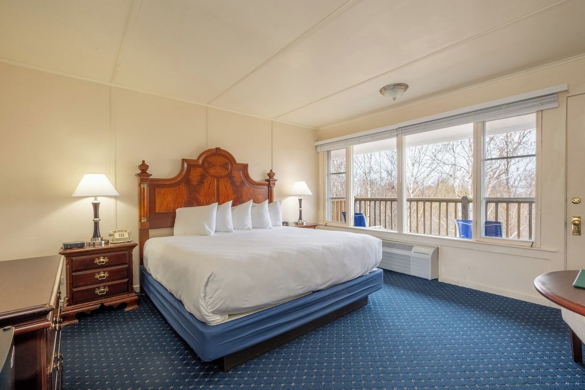 Habitación de hotel con una cama grande, dos mesitas de noche, un aparador, una ventana con vistas y una lámpara de techo.