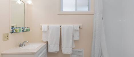 Un bagno con lavandino, specchio, porta asciugamani, finestra e doccia.