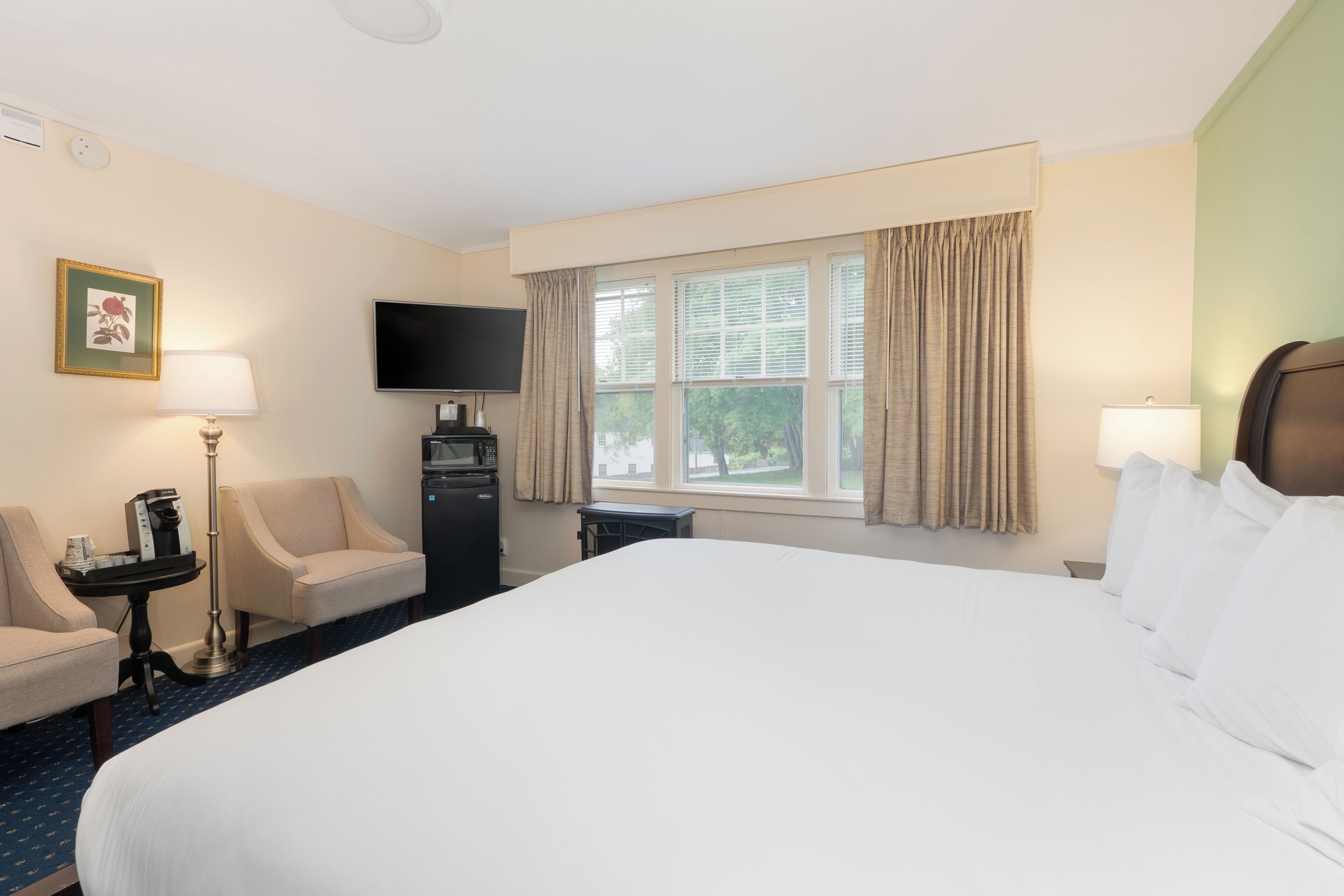 Habitación de hotel con una cama grande, un escritorio con lámpara, un televisor y una ventana con cortinas.