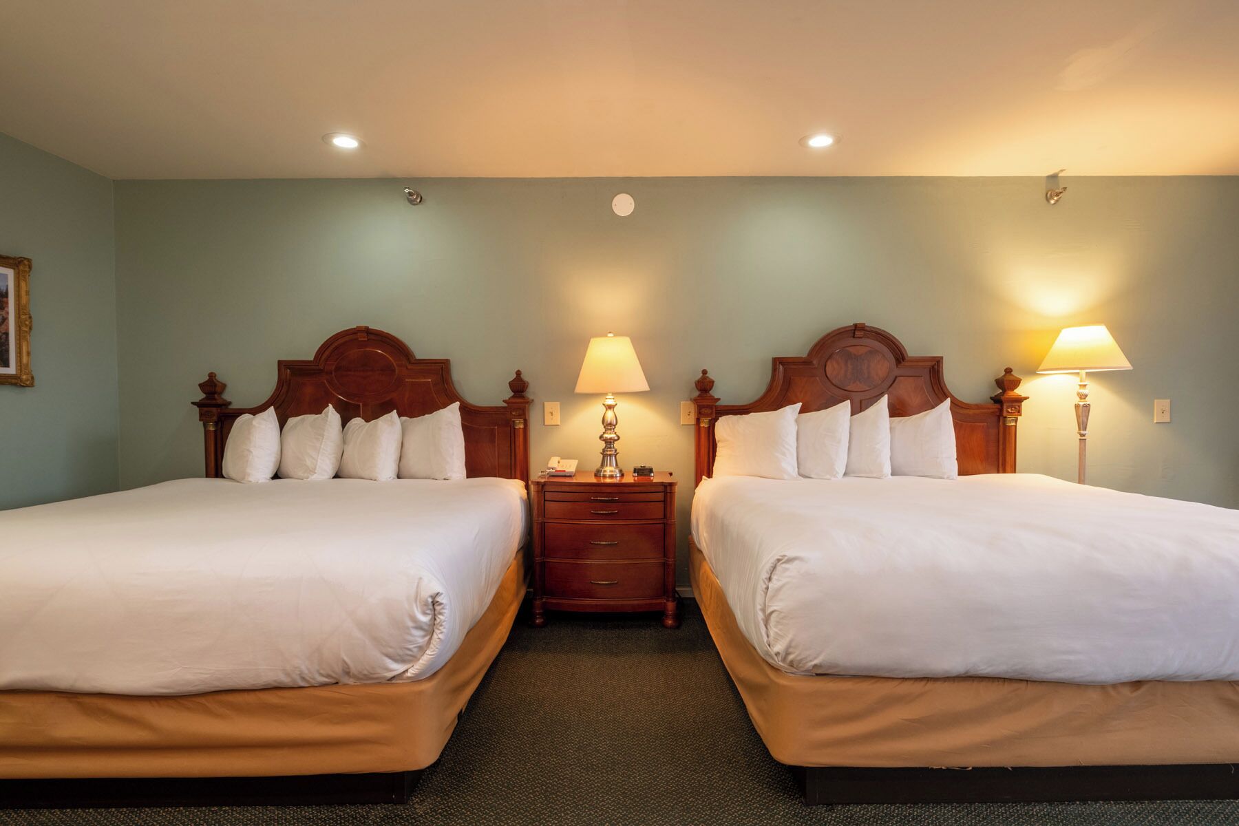 Habitación de hotel con dos camas, una mesita de noche y una lámpara entre ellas.
