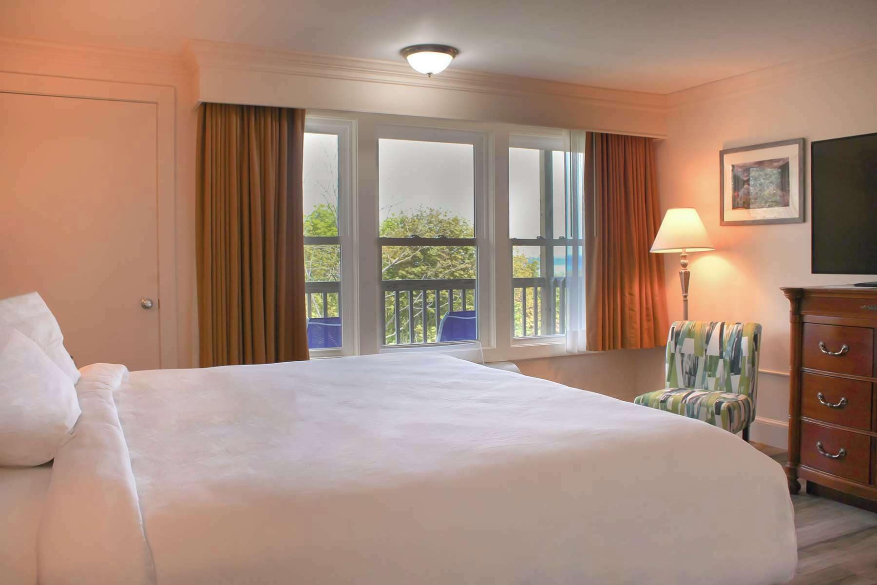 Een hotelkamer met een groot bed, een stoel, een kast en een raam met gordijnen.