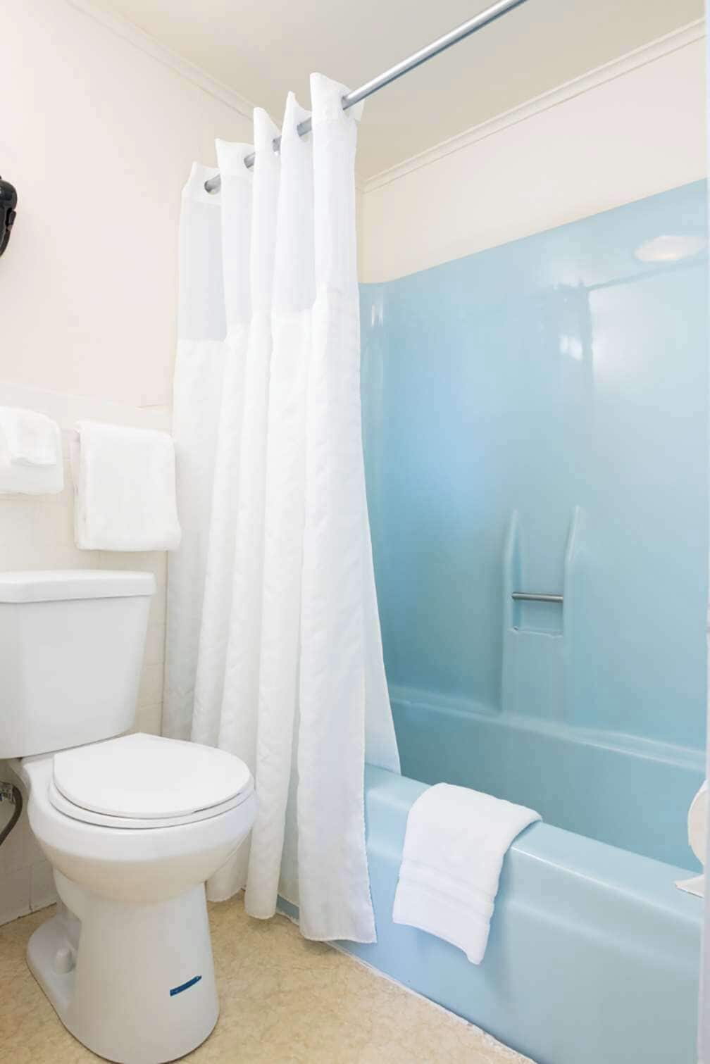 Un baño con inodoro blanco, bañera con cabina de ducha azul y toalla colgada en la pared.