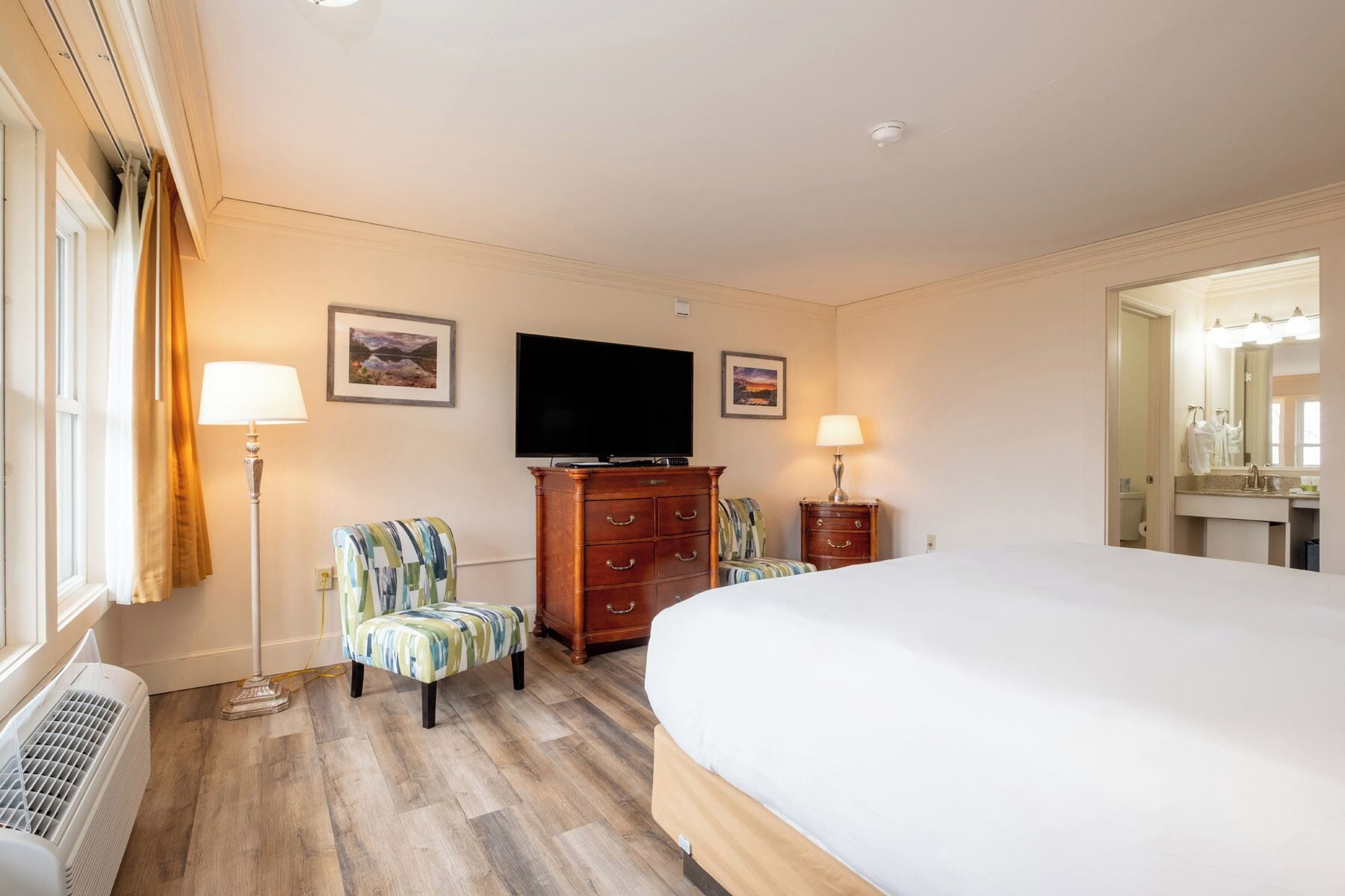 Una habitación de hotel con una cama grande, dos sillas, un televisor y un aparador.