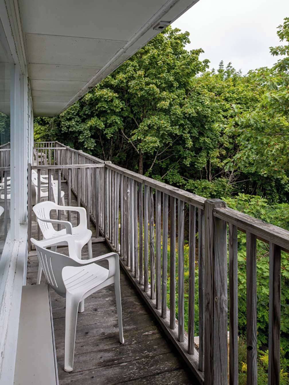 A wooden deck with white plastic chairs, surrounded by lush greenery.