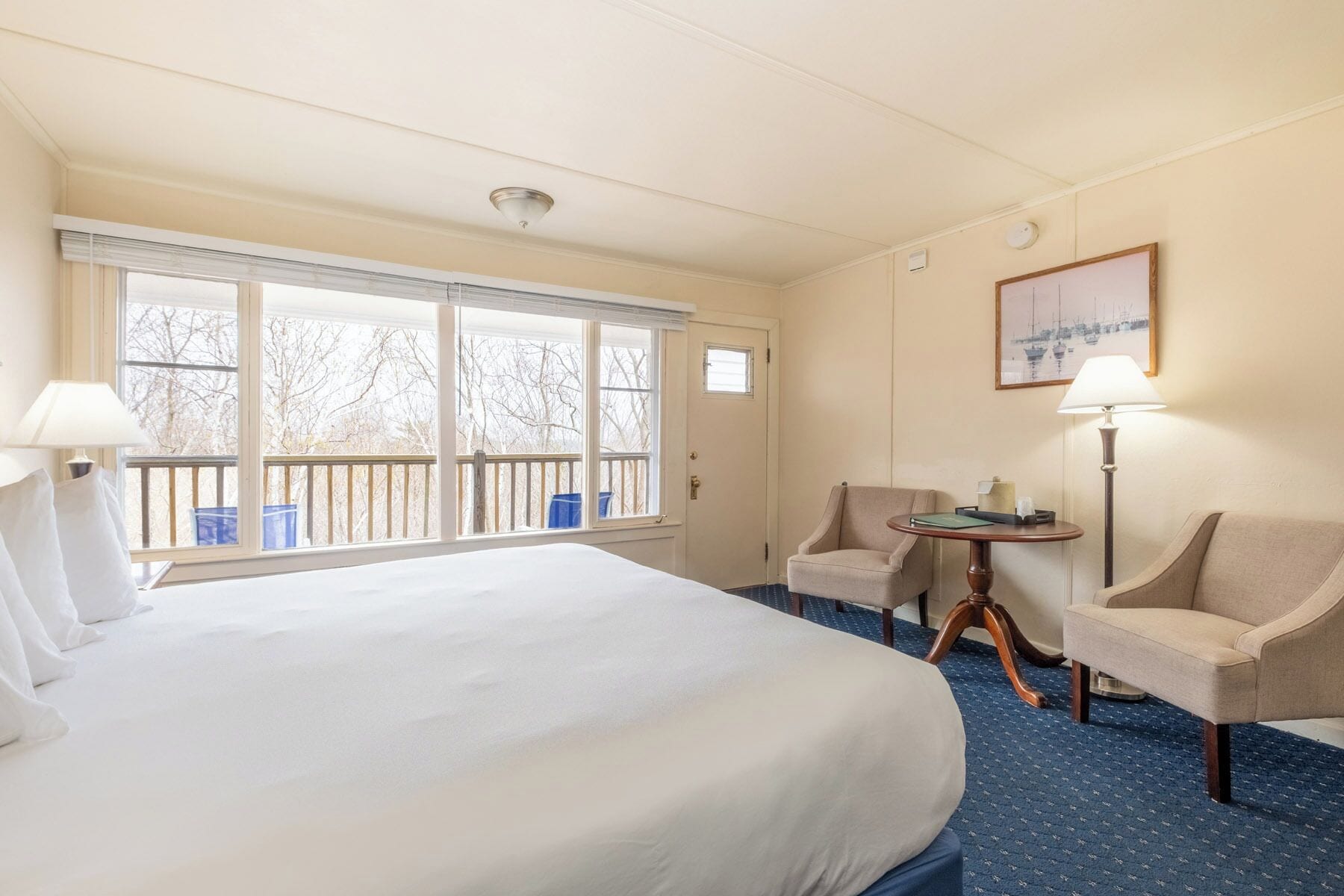 Habitación de hotel con una cama grande, dos sillones, una mesita y vistas a árboles a través de las ventanas.