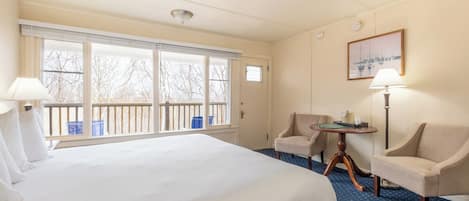 Habitación de hotel con una cama grande, dos sillones, una mesita y vistas a árboles a través de las ventanas.