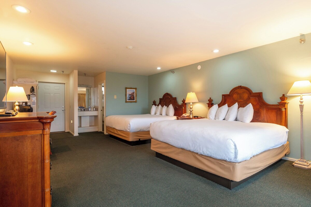 Une chambre d’hôtel avec deux lits, un bureau, un miroir et une porte donnant sur une salle de bain.