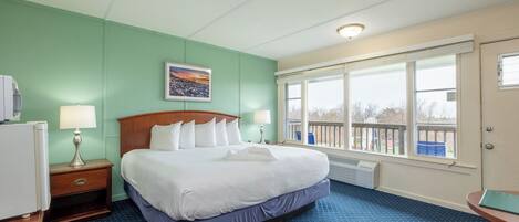Une chambre d’hôtel avec un lit, deux tables de chevet, une fenêtre donnant sur un beau paysage et un tableau au mur.