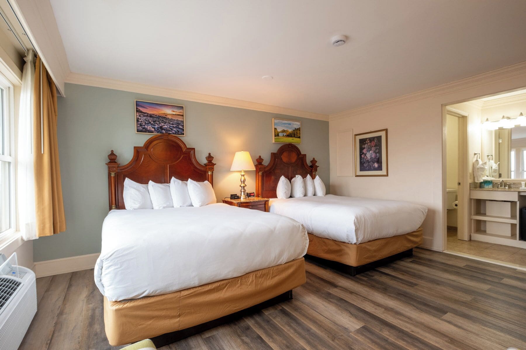 A hotel room with two beds, a nightstand, a lamp, and a painting on the wall.