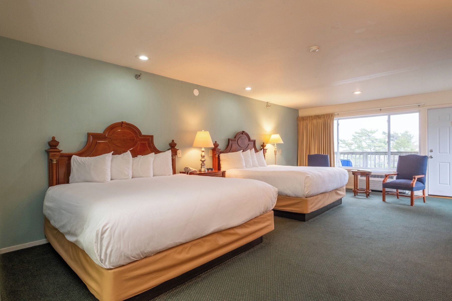 Habitación de hotel con dos camas, una mesita, una silla y un balcón.