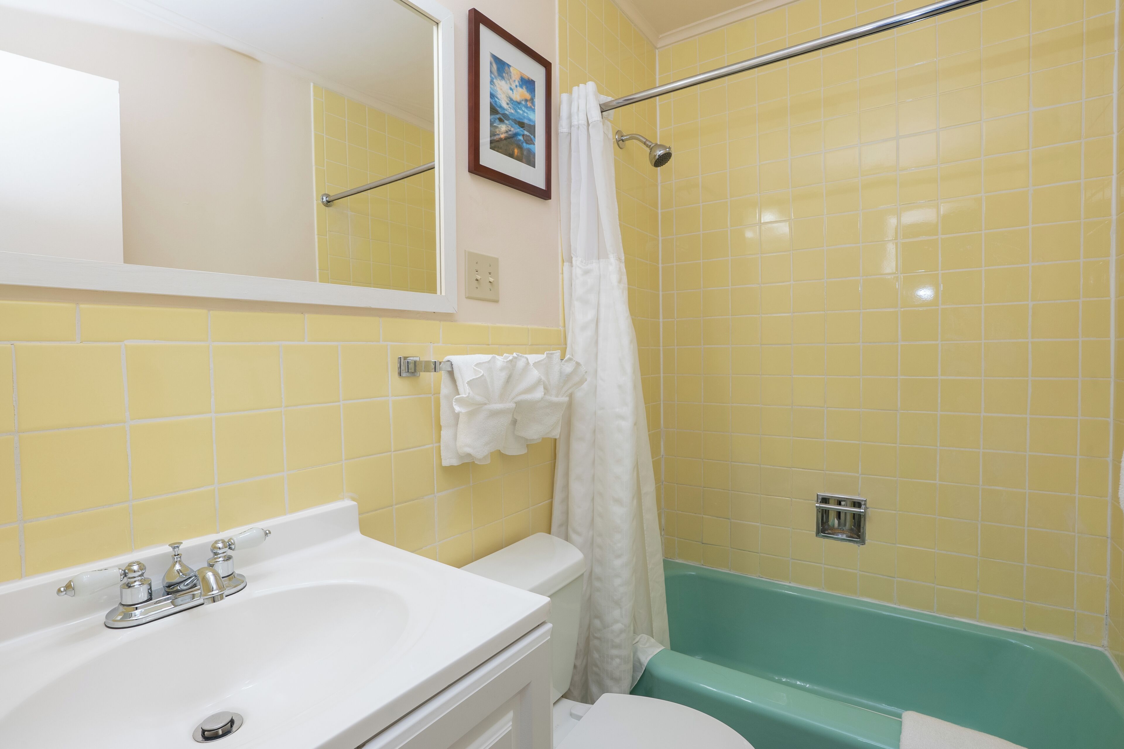 A bathroom with yellow tiles, a white sink, a green bathtub, and a white shower curtain.