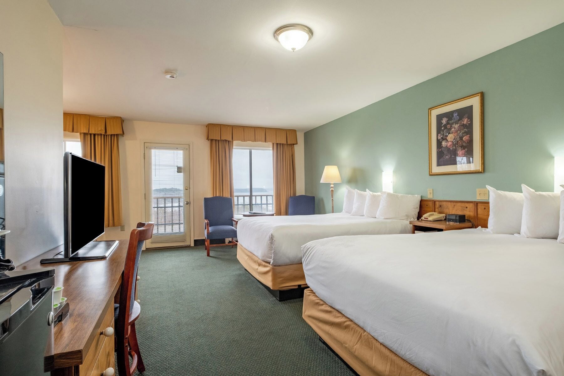 A hotel room with two beds, a desk with a television, a chair, a lamp, and a painting on the wall.