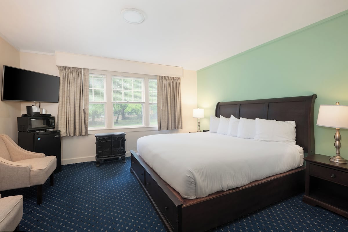 Habitación de hotel con una cama grande, televisor, escritorio con microondas y ventana con cortinas.