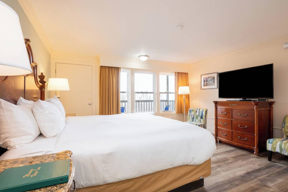 Habitación de hotel con cama, televisión, cómoda y balcón con cortinas.