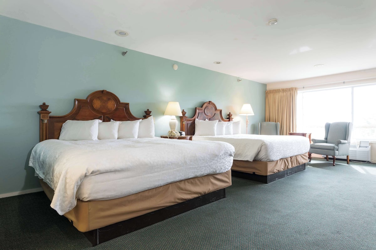Habitación de hotel con dos camas, una silla y un ventanal grande.