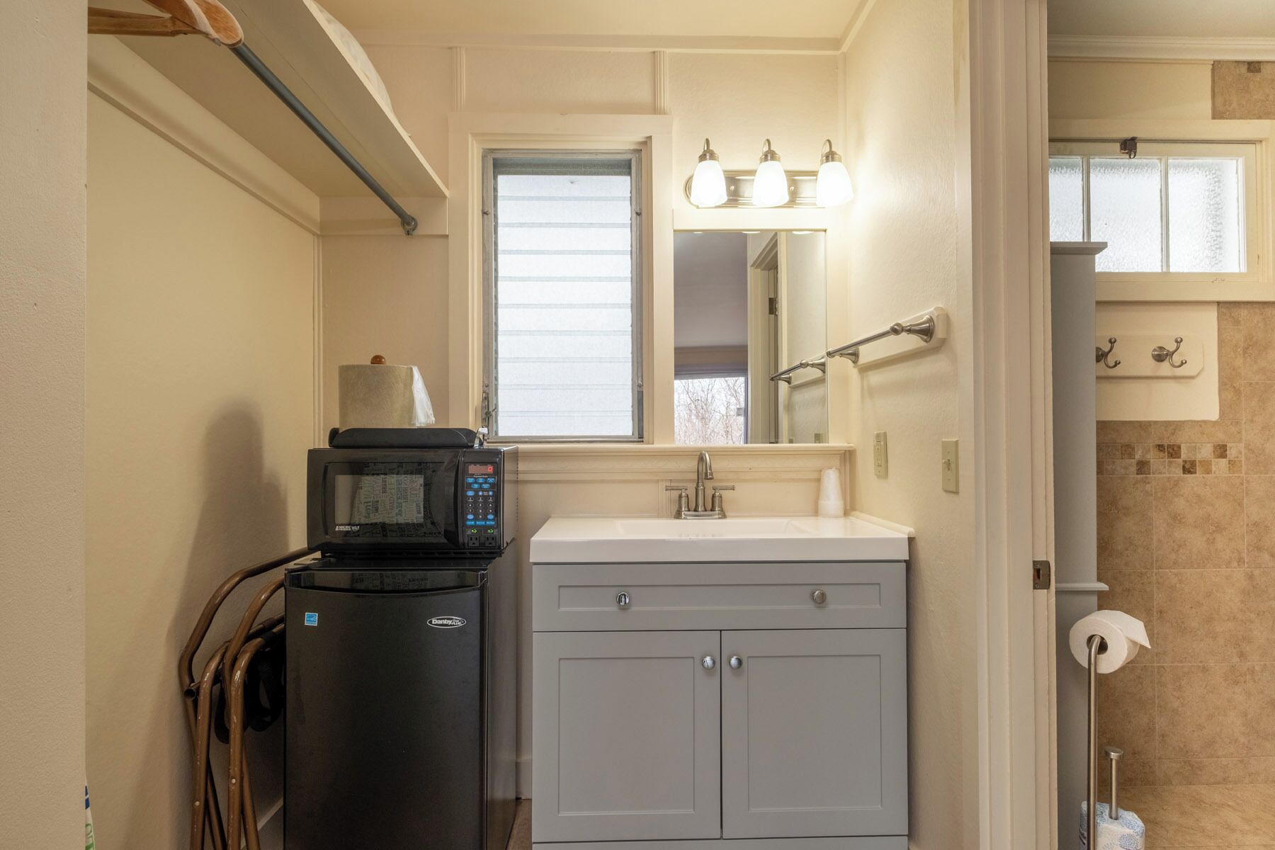 A bathroom with a sink, mirror, towel rack, and a microwave on a stand.