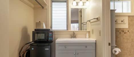 A bathroom with a sink, mirror, towel rack, and a microwave on a stand.