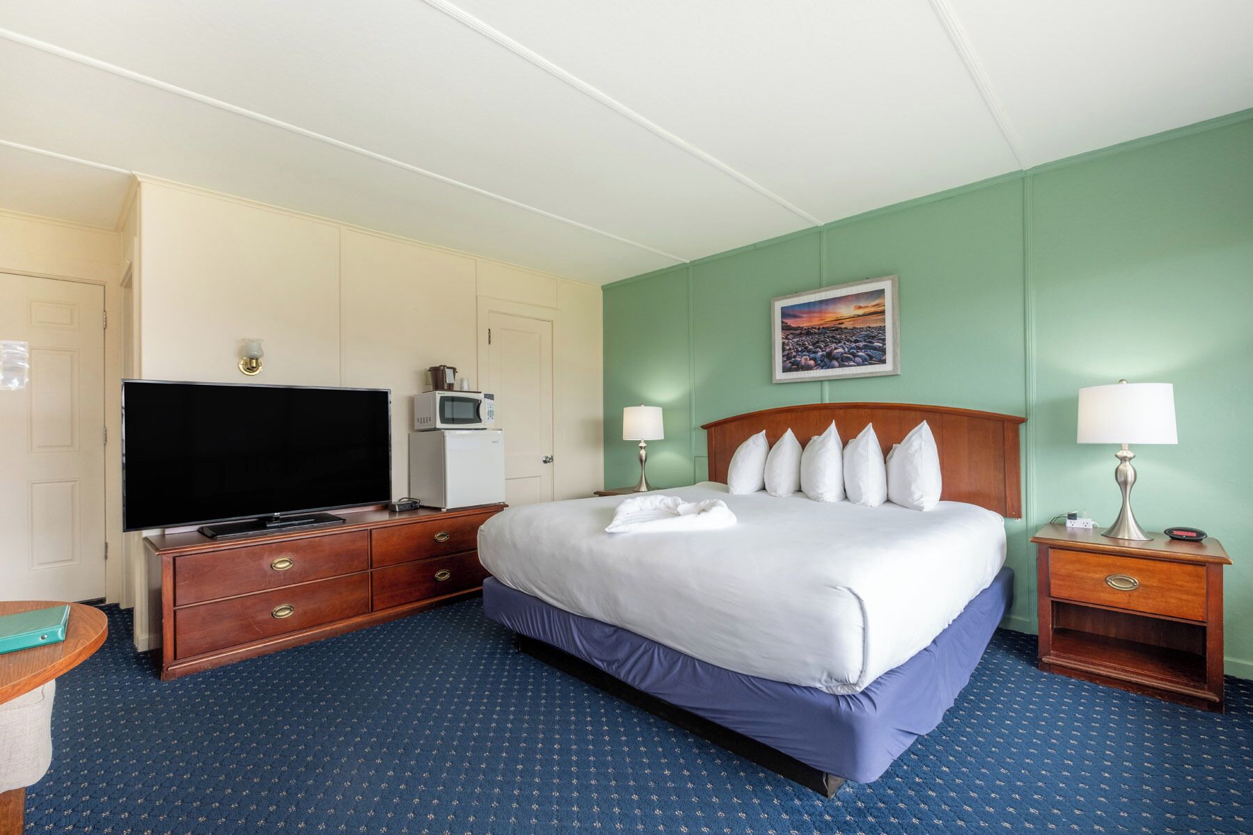 A hotel room with a bed, a TV, a microwave, a desk, and a nightstand.